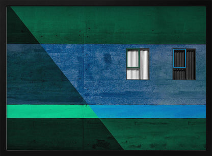 A framed abstract architectural photograph featuring a color-blocked facade. A central horizontal band of textured blue wall contains two small, distinct windows. This is flanked by upper and lower sections of dark green. A large, dark diagonal shape overlays the left side of the composition, creating sharp geometric lines. Decor