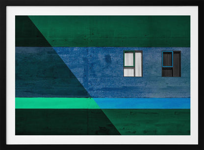 A framed abstract architectural photograph featuring a color-blocked facade. A central horizontal band of textured blue wall contains two small, distinct windows. This is flanked by upper and lower sections of dark green. A large, dark diagonal shape overlays the left side of the composition, creating sharp geometric lines. Decor