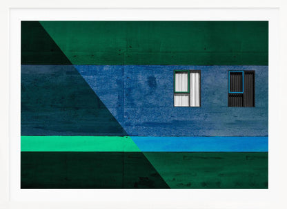 A framed abstract architectural photograph featuring a color-blocked facade. A central horizontal band of textured blue wall contains two small, distinct windows. This is flanked by upper and lower sections of dark green. A large, dark diagonal shape overlays the left side of the composition, creating sharp geometric lines. Decor