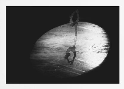 A dramatic black and white framed photograph of a female figure skater performing on ice. She is illuminated by a single spotlight, holding a graceful standing split pose, with her reflection visible on the ice below. Poster