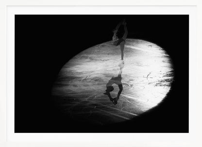 A dramatic black and white framed photograph of a female figure skater performing on ice. She is illuminated by a single spotlight, holding a graceful standing split pose, with her reflection visible on the ice below. Poster