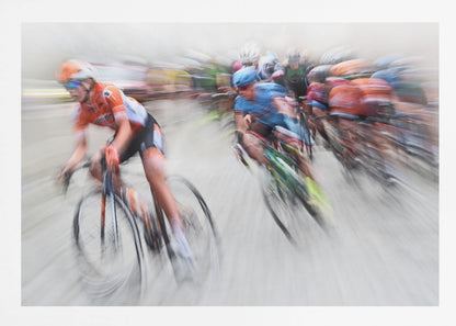 An action photograph of a professional cycling race captured with a prominent motion blur effect that conveys a strong sense of speed. A cyclist in an orange and black uniform is in the foreground, leaning into a turn, while a group of other riders in blue and multi-colored jerseys follows closely behind, their forms streaked and blurred. The entire scene is encased in a brushed silver frame. Poster