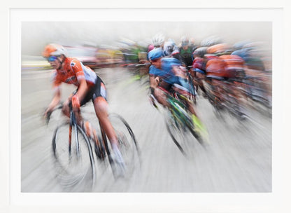 An action photograph of a professional cycling race captured with a prominent motion blur effect that conveys a strong sense of speed. A cyclist in an orange and black uniform is in the foreground, leaning into a turn, while a group of other riders in blue and multi-colored jerseys follows closely behind, their forms streaked and blurred. The entire scene is encased in a brushed silver frame. Poster