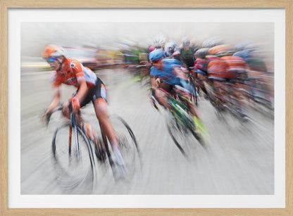 An action photograph of a professional cycling race captured with a prominent motion blur effect that conveys a strong sense of speed. A cyclist in an orange and black uniform is in the foreground, leaning into a turn, while a group of other riders in blue and multi-colored jerseys follows closely behind, their forms streaked and blurred. The entire scene is encased in a brushed silver frame. Poster