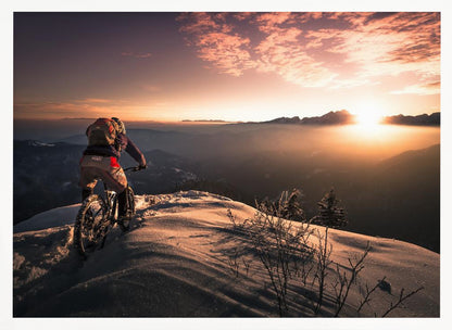 A mountain biker seen from behind pauses on a snowy mountain summit, overlooking a vast, misty mountain range as the sun sets, casting a warm orange and pink glow across the sky and snow. Artwork
