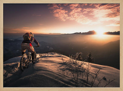 A mountain biker seen from behind pauses on a snowy mountain summit, overlooking a vast, misty mountain range as the sun sets, casting a warm orange and pink glow across the sky and snow. Artwork