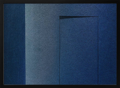 An abstract geometric artwork featuring textured panels in various shades of deep and dusty blue. The composition is divided into vertical sections, with a central rectangular shape that appears slightly recessed, creating a strong shadow line at its top edge. The piece is enclosed in a simple, brushed silver frame. Wall Art
