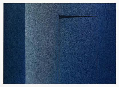 An abstract geometric artwork featuring textured panels in various shades of deep and dusty blue. The composition is divided into vertical sections, with a central rectangular shape that appears slightly recessed, creating a strong shadow line at its top edge. The piece is enclosed in a simple, brushed silver frame. Wall Art