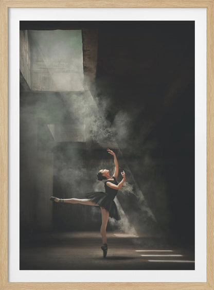 A ballerina in a black tutu gracefully performs an arabesque in a vast, dark, industrial space filled with smoke, dramatically illuminated by shafts of light from above. Poster