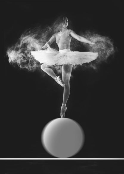 A dramatic black and white photograph of a ballerina balancing on one pointe shoe on top of a large sphere. She wears a white tutu and is surrounded by a cloud of white powder, capturing a moment of explosive, graceful movement against a solid black background. Wall Art
