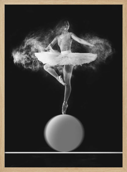 A dramatic black and white photograph of a ballerina balancing on one pointe shoe on top of a large sphere. She wears a white tutu and is surrounded by a cloud of white powder, capturing a moment of explosive, graceful movement against a solid black background. Wall Art