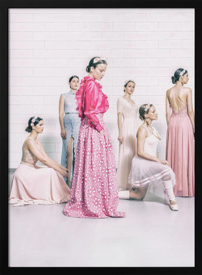 A studio photograph of six young women in elegant pastel gowns posing against a white brick wall. The central figure wears a vibrant pink ruffled blouse and a patterned maxi skirt, while the others are dressed in light pink, white, and pale blue dresses, some with ballet-inspired elements. They all have flowers in their hair, creating a soft, high-fashion aesthetic. Print