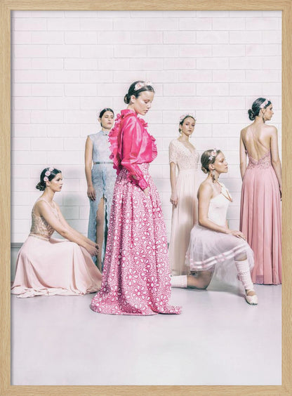 A studio photograph of six young women in elegant pastel gowns posing against a white brick wall. The central figure wears a vibrant pink ruffled blouse and a patterned maxi skirt, while the others are dressed in light pink, white, and pale blue dresses, some with ballet-inspired elements. They all have flowers in their hair, creating a soft, high-fashion aesthetic. Print