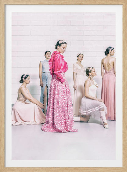 A studio photograph of six young women in elegant pastel gowns posing against a white brick wall. The central figure wears a vibrant pink ruffled blouse and a patterned maxi skirt, while the others are dressed in light pink, white, and pale blue dresses, some with ballet-inspired elements. They all have flowers in their hair, creating a soft, high-fashion aesthetic. Print