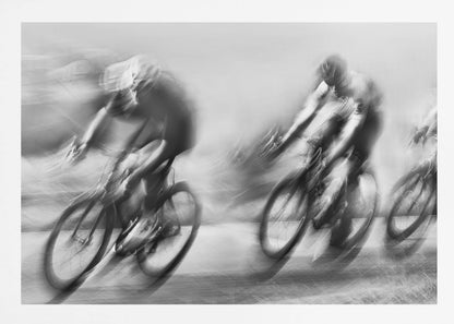 A dynamic black and white action photograph of three cyclists racing, captured with a slow shutter speed to create a dramatic motion blur effect. The riders and their bikes are blurred into streaks of light and shadow, conveying a powerful sense of speed and intensity. The image is presented within a silver-toned frame. Poster