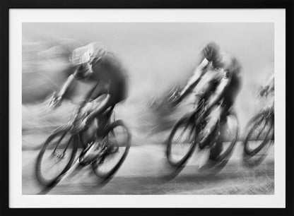 A dynamic black and white action photograph of three cyclists racing, captured with a slow shutter speed to create a dramatic motion blur effect. The riders and their bikes are blurred into streaks of light and shadow, conveying a powerful sense of speed and intensity. The image is presented within a silver-toned frame. Poster