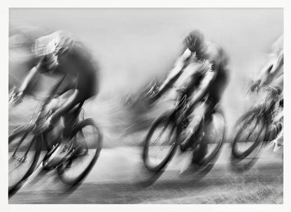 A dynamic black and white action photograph of three cyclists racing, captured with a slow shutter speed to create a dramatic motion blur effect. The riders and their bikes are blurred into streaks of light and shadow, conveying a powerful sense of speed and intensity. The image is presented within a silver-toned frame. Poster