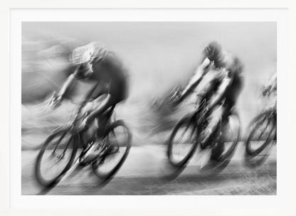 A dynamic black and white action photograph of three cyclists racing, captured with a slow shutter speed to create a dramatic motion blur effect. The riders and their bikes are blurred into streaks of light and shadow, conveying a powerful sense of speed and intensity. The image is presented within a silver-toned frame. Poster
