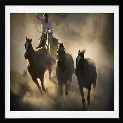 A dramatic, backlit photograph of a cowboy on horseback herding a small group of horses, kicking up a large cloud of dust as they gallop through a rustic landscape at sunrise or sunset. Poster