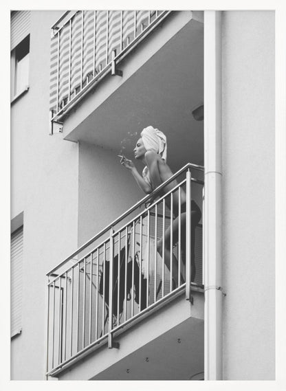 A black and white photo of a woman with a towel on her head, smoking a cigarette on an apartment balcony. The low-angle shot captures her leaning on the metal railing, with smoke drifting from the cigarette. Print
