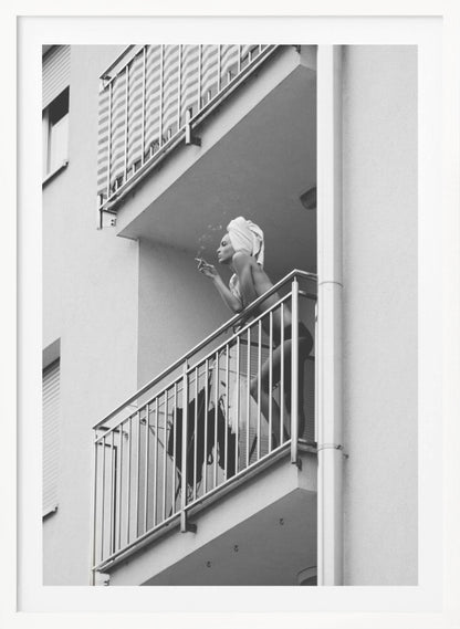 A black and white photo of a woman with a towel on her head, smoking a cigarette on an apartment balcony. The low-angle shot captures her leaning on the metal railing, with smoke drifting from the cigarette. Print