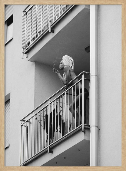 A black and white photo of a woman with a towel on her head, smoking a cigarette on an apartment balcony. The low-angle shot captures her leaning on the metal railing, with smoke drifting from the cigarette. Print
