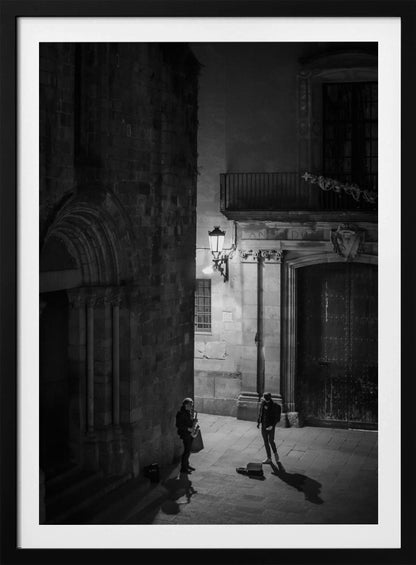 A high-angle, black and white photograph of a street musician playing a saxophone for a lone listener in a narrow stone alley at night. The scene is illuminated by an ornate streetlamp, casting long shadows on the cobblestone ground. Wall Art