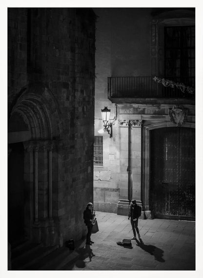 A high-angle, black and white photograph of a street musician playing a saxophone for a lone listener in a narrow stone alley at night. The scene is illuminated by an ornate streetlamp, casting long shadows on the cobblestone ground. Wall Art