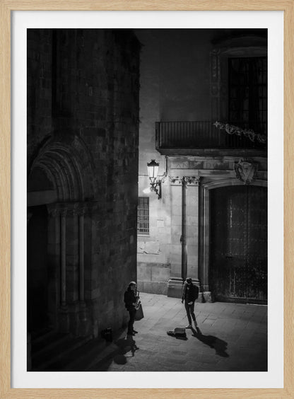 A high-angle, black and white photograph of a street musician playing a saxophone for a lone listener in a narrow stone alley at night. The scene is illuminated by an ornate streetlamp, casting long shadows on the cobblestone ground. Wall Art
