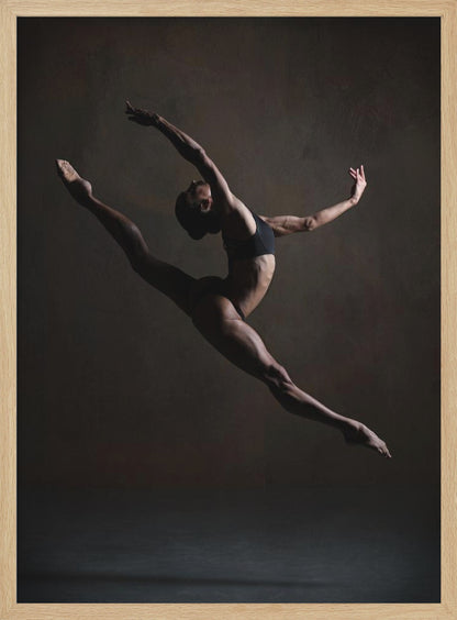 A dramatic, low-key studio photograph of a muscular female dancer captured mid-leap. She is in a full split, arching her back with her arms extended gracefully. The lighting accentuates her toned physique against a dark, textured brown background. Poster