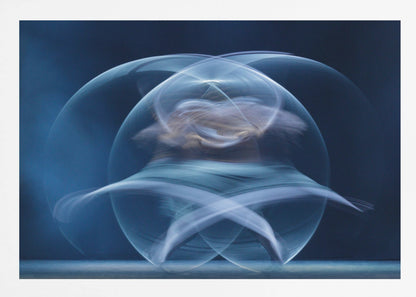 An abstract long-exposure photograph of a spinning dancer, creating ethereal, intersecting trails of blue and white light that form a glowing, orb-like shape against a deep blue background. The image is presented within a silver frame. Poster