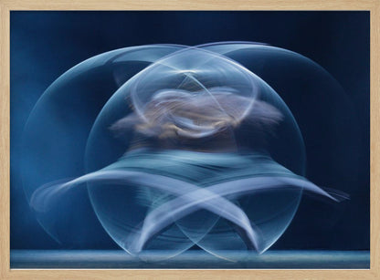 An abstract long-exposure photograph of a spinning dancer, creating ethereal, intersecting trails of blue and white light that form a glowing, orb-like shape against a deep blue background. The image is presented within a silver frame. Poster