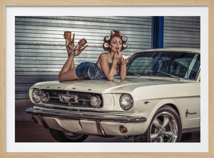 A woman in a retro pin-up style lies on the hood of a vintage white Ford Mustang in a garage, applying red lipstick with her hair set in soda can curlers. Poster