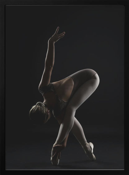A dramatic studio photograph of a ballerina in a complex pose against a solid black background. Strong rim lighting highlights the graceful curves of her body as she bends forward with her legs crossed, one arm extended high and the other reaching towards her pointe shoes. Poster