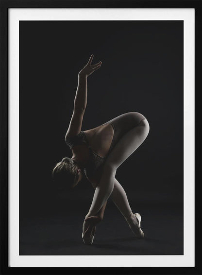 A dramatic studio photograph of a ballerina in a complex pose against a solid black background. Strong rim lighting highlights the graceful curves of her body as she bends forward with her legs crossed, one arm extended high and the other reaching towards her pointe shoes. Poster