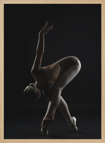 A dramatic studio photograph of a ballerina in a complex pose against a solid black background. Strong rim lighting highlights the graceful curves of her body as she bends forward with her legs crossed, one arm extended high and the other reaching towards her pointe shoes. Poster