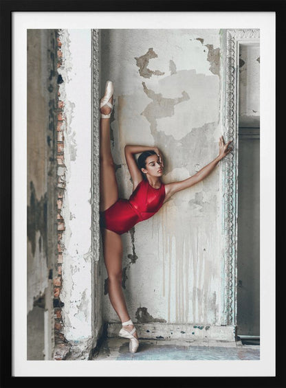 A ballerina in a shiny red leotard performs a standing split against a distressed, peeling wall. Her left leg is extended straight up, and her body leans against the wall in a display of incredible flexibility and grace amidst a rustic, derelict setting. Artwork