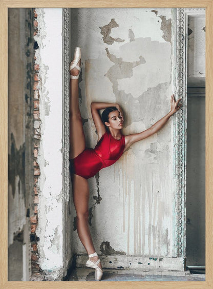 A ballerina in a shiny red leotard performs a standing split against a distressed, peeling wall. Her left leg is extended straight up, and her body leans against the wall in a display of incredible flexibility and grace amidst a rustic, derelict setting. Artwork