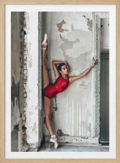 A ballerina in a shiny red leotard performs a standing split against a distressed, peeling wall. Her left leg is extended straight up, and her body leans against the wall in a display of incredible flexibility and grace amidst a rustic, derelict setting. Artwork