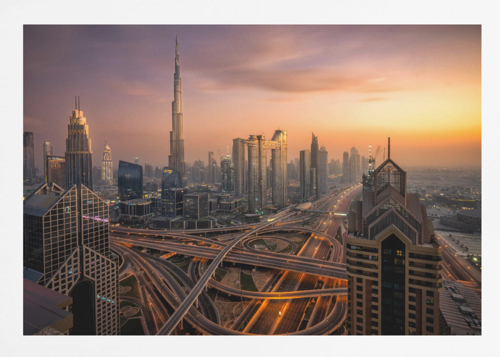 An elevated photograph of the Dubai skyline at sunset, featuring the towering Burj Khalifa against a hazy orange and purple sky. In the foreground, a complex network of illuminated highways and overpasses weaves between modern skyscrapers. Wall Art