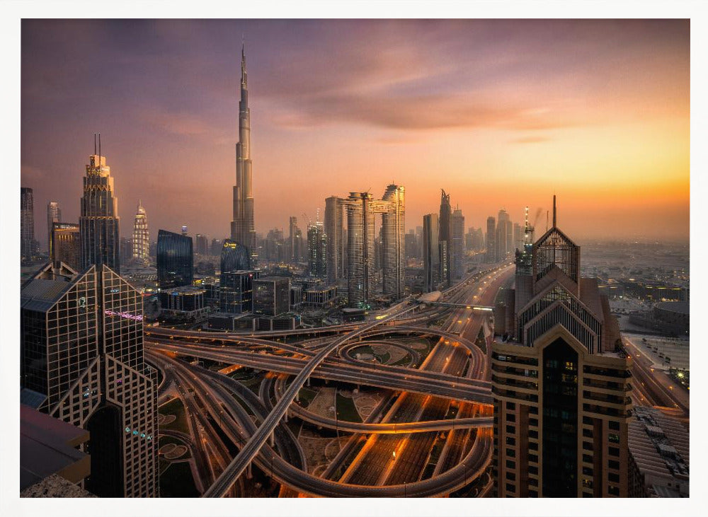 An elevated photograph of the Dubai skyline at sunset, featuring the towering Burj Khalifa against a hazy orange and purple sky. In the foreground, a complex network of illuminated highways and overpasses weaves between modern skyscrapers. Wall Art