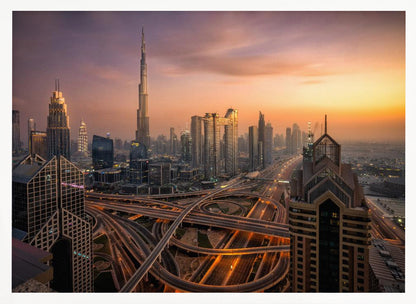 An elevated photograph of the Dubai skyline at sunset, featuring the towering Burj Khalifa against a hazy orange and purple sky. In the foreground, a complex network of illuminated highways and overpasses weaves between modern skyscrapers. Wall Art