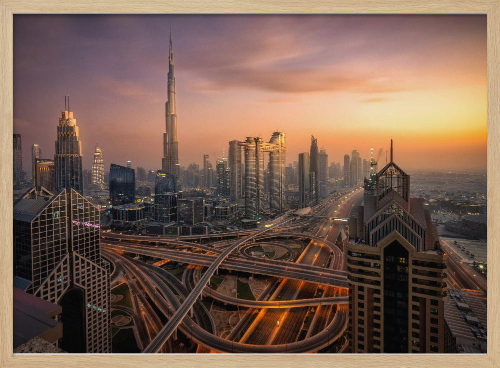An elevated photograph of the Dubai skyline at sunset, featuring the towering Burj Khalifa against a hazy orange and purple sky. In the foreground, a complex network of illuminated highways and overpasses weaves between modern skyscrapers. Wall Art