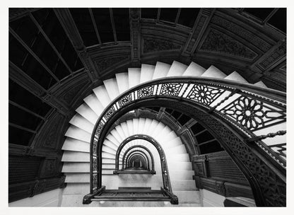 A mesmerizing black and white photograph shot from a high angle looking down into the center of a spiral staircase. The bright white marble steps contrast with the dark, ornate metal railing, creating a repeating arched pattern that draws the eye downward into a seemingly endless tunnel. The image is presented within a silver-colored frame. Artwork
