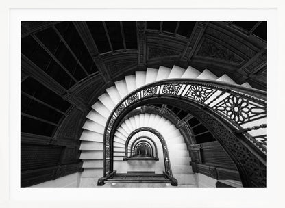 A mesmerizing black and white photograph shot from a high angle looking down into the center of a spiral staircase. The bright white marble steps contrast with the dark, ornate metal railing, creating a repeating arched pattern that draws the eye downward into a seemingly endless tunnel. The image is presented within a silver-colored frame. Artwork