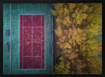 An aerial top-down photograph of a red and green tennis court covered in fallen leaves, adjacent to a dense grove of trees with vibrant yellow and gold autumn foliage, all enclosed in a silver frame. Wall Art