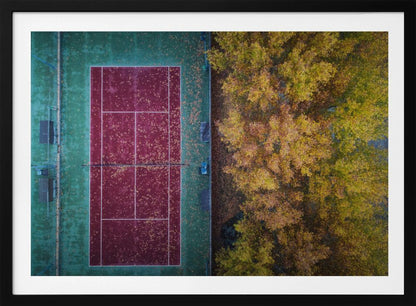 An aerial top-down photograph of a red and green tennis court covered in fallen leaves, adjacent to a dense grove of trees with vibrant yellow and gold autumn foliage, all enclosed in a silver frame. Wall Art