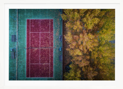An aerial top-down photograph of a red and green tennis court covered in fallen leaves, adjacent to a dense grove of trees with vibrant yellow and gold autumn foliage, all enclosed in a silver frame. Wall Art