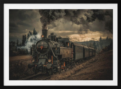 A powerful black steam locomotive on a railway track, billowing thick dark smoke into a dramatic, cloudy sky. The train travels through a rustic, grassy landscape, and the image has a warm, vintage color tone, all within a silver frame. Wall Art