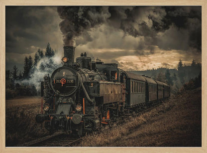 A powerful black steam locomotive on a railway track, billowing thick dark smoke into a dramatic, cloudy sky. The train travels through a rustic, grassy landscape, and the image has a warm, vintage color tone, all within a silver frame. Wall Art